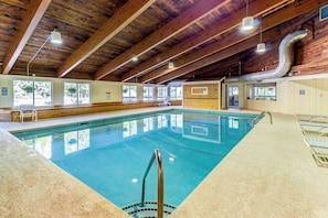 Ein Innenpool mit Holzbalken, großen Fenstern und gefliestem Boden.