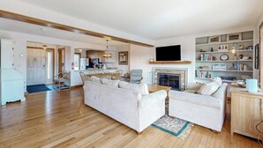 A living room with a sofa, a television, a fireplace, and a bookshelf. - Saltbox townhome with views & fireplace - near Quechee Club, golf, & skiing (White River Junction)