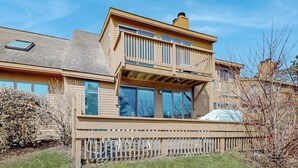 A two-story house with a balcony, large windows, and a fenced yard. - Saltbox townhome with views & fireplace - near Quechee Club, golf, & skiing (White River Junction)
