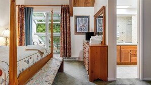 Une chambre à coucher avec un lit à baldaquin, une commode en bois et une vue sur la salle de bain.