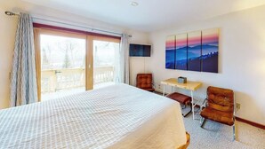A bedroom with a large bed, a desk, a chair, and a TV.