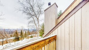 A wooden balcony with a view of a snowy landscape and distant buildings.