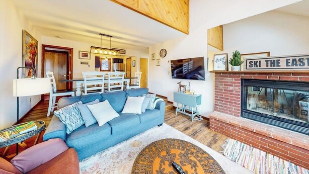 A living room with a blue sofa, a fireplace, and a dining area with a wooden ceiling.