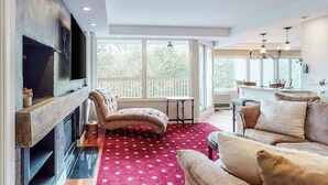 Ein Wohnzimmer mit Kamin, einer Couch, einem roten Teppich mit Muster und großen Fenstern.