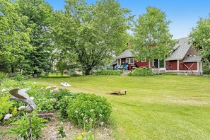 Une maison rouge avec une pelouse bien entretenue et un jardin agrémenté de fleurs et d’un abreuvoir pour les oiseaux.