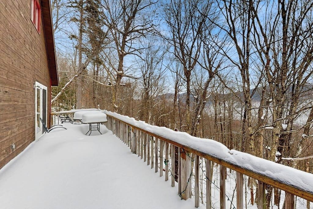 A wooden deck with a snow-covered railing, a bench, and a table.