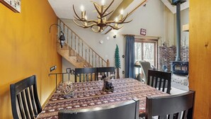 Ein Essbereich mit einer Chandelier, Holzstühlen, einer gemusterten Tischdecke und einer Treppe, die zu einem anderen Raum führt.