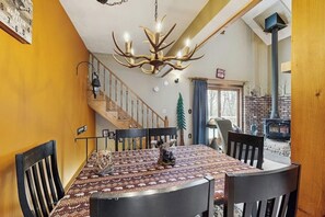 Ein Essbereich mit einer Chandelier, Holzstühlen, einer gemusterten Tischdecke und einer Treppe, die zu einem anderen Raum führt.