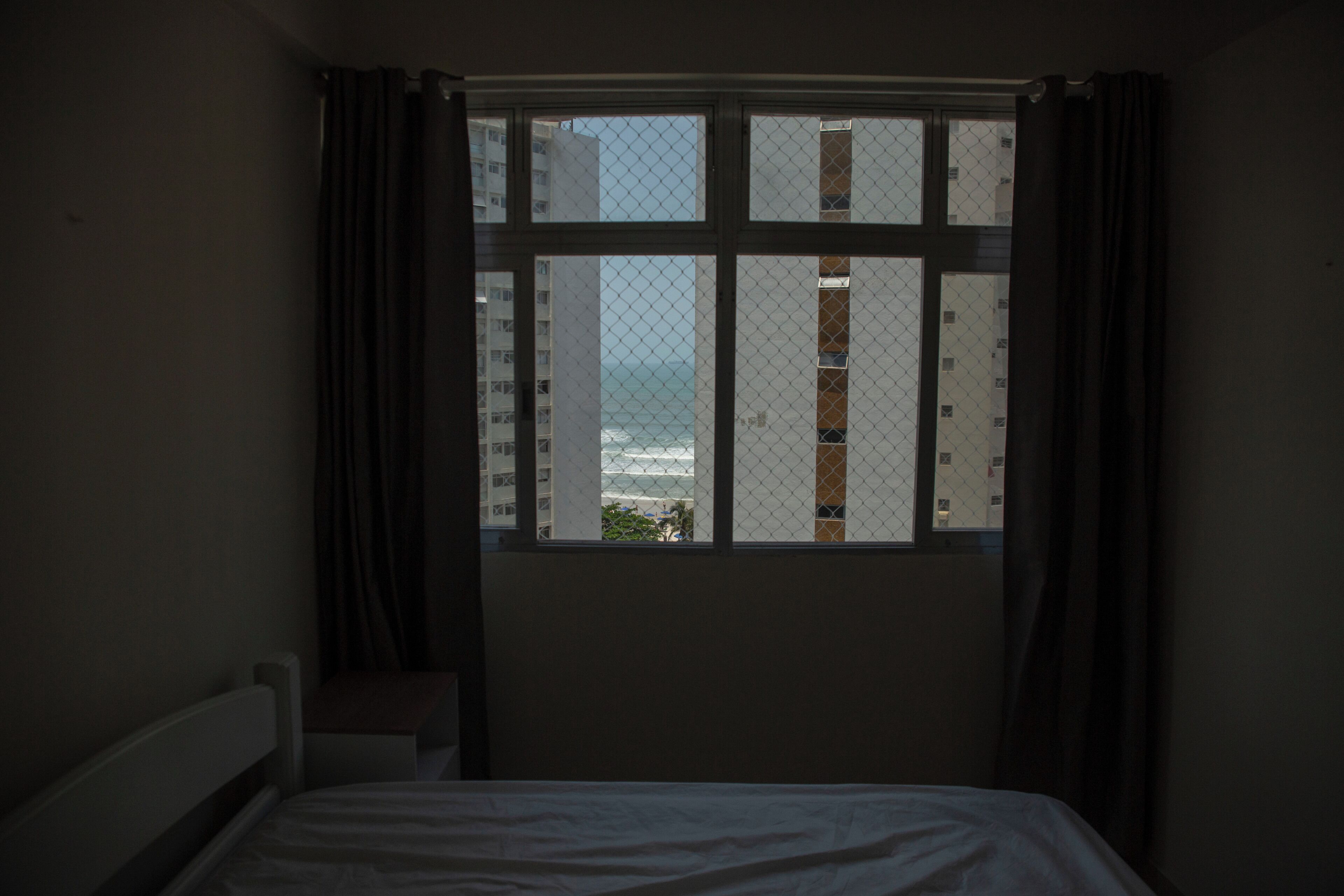 Quarto com cama, janela com cortinas e vista para edifícios e um corpo de água.