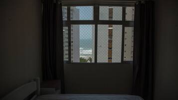 Quarto com cama, janela com cortinas e vista para edifícios e um corpo de água.