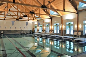 Ein Hallenbad mit Holzbalkendecke, Liegestühlen und großen Fenstern.