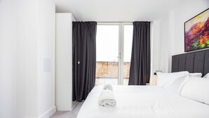 Hotellihuone, jossa on sänky, ikkuna verhoilla, taulu seinällä ja näkymä ulos.