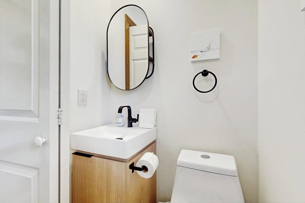 Ein Badezimmer mit einem weißen Waschbecken, einem Spiegel, einer Toilette und einem Handtuchspender.