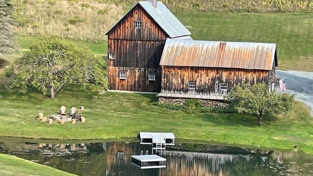 Un granero rústico con techo de metal, un pequeño muelle y un estanque en un entorno rural.