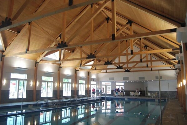 An indoor swimming pool with wooden beams, clear windows, and a tiled floor.