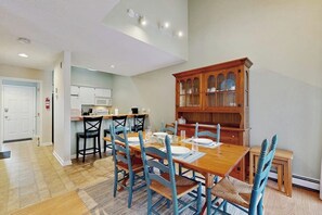 A dining area with a wooden table and blue chairs, a kitchen with white cabinets, and a wooden cabinet with glass doors.