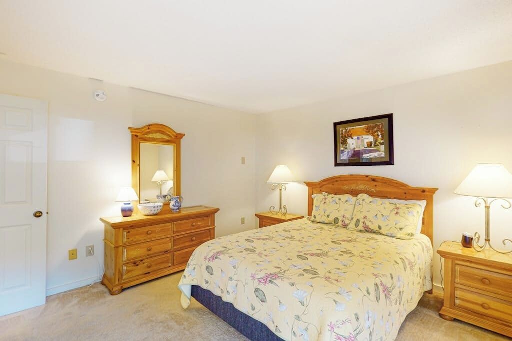 Ein Schlafzimmer mit einem Bett, zwei Nachttischen, einer Kommode, einem Spiegel und einem gerahmten Bild an der Wand.