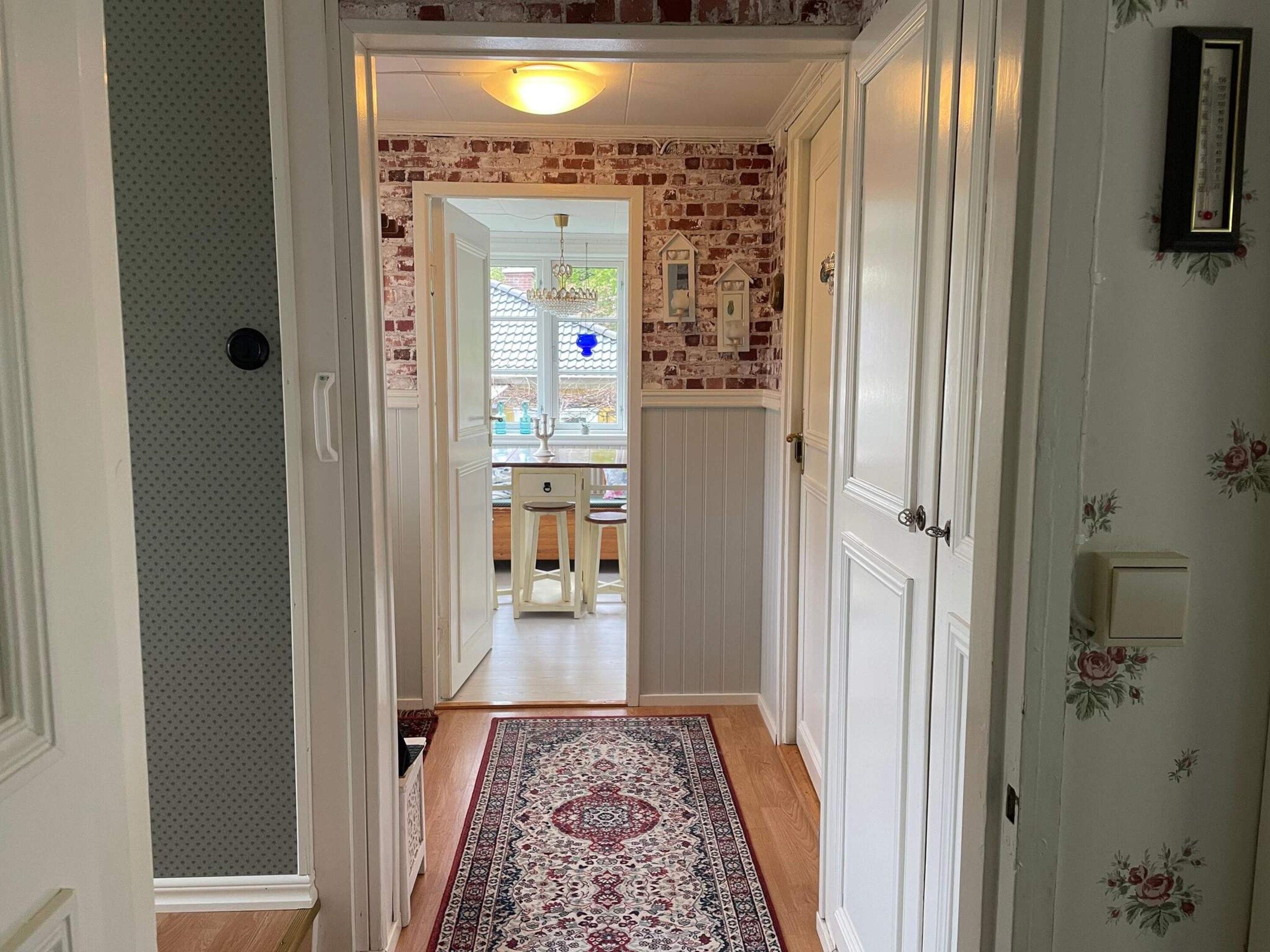 Ein Flur mit einem gemusterten Teppich, einer Ziegelwand und einer Tür, die zu einem Raum mit einem Fenster und einem Chandelier führt.