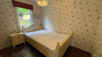 Une chambre à coucher comprenant un lit, une table de chevet, une lampe, une fenêtre agrémentée d’une lambrequin rouge et un lustre.