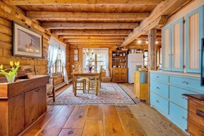Interior de una cabaña de troncos con una mesa de comedor de madera, sillas, un mueble azul y suelo de madera.