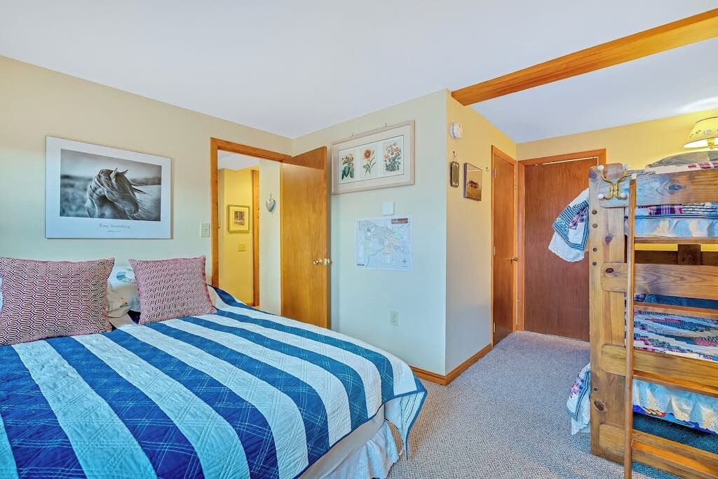 A bedroom with a bed, a bunk bed, a door, and a wall with a map and a framed picture.