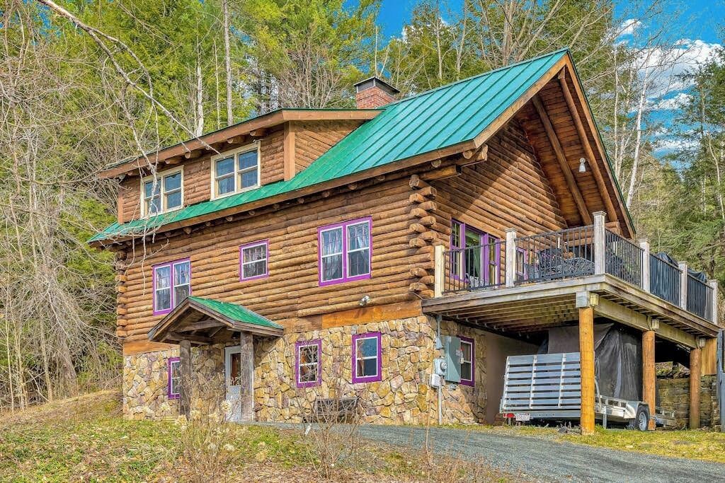 A log cabin with a stone foundation, multiple windows, and a green roof.