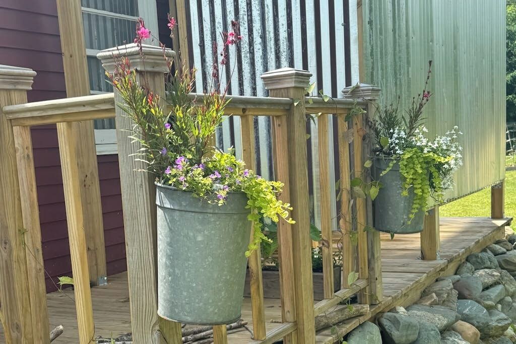 Une terrasse en bois agrémentée de jardinières en métal où sont plantées des fleurs.