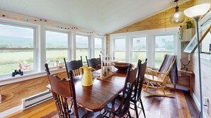 A dining area with a wooden table, chairs, and a view of the outdoors through large windows. - Historic home on 1 acre with snowmobile trails in backyard & mountain views (Waitsfield)