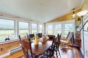 Un espace repas avec une table en bois, des chaises et une vue sur l’extérieur grâce à de grandes fenêtres.