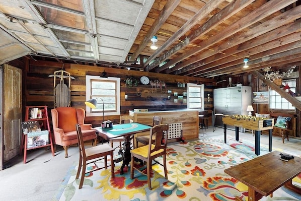 A rustic interior with wooden beams, a dining area with chairs, a table, and a colorful rug.