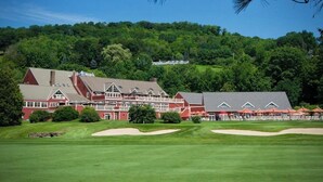A large building with multiple stories and a red roof, surrounded by a well-maintained lawn and sand bunkers. - Quechee Condo | Condo in Quechee (Quechee)
