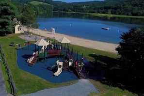Uma área de recreação infantil com escorregadores e estruturas de escalada perto de um lago.