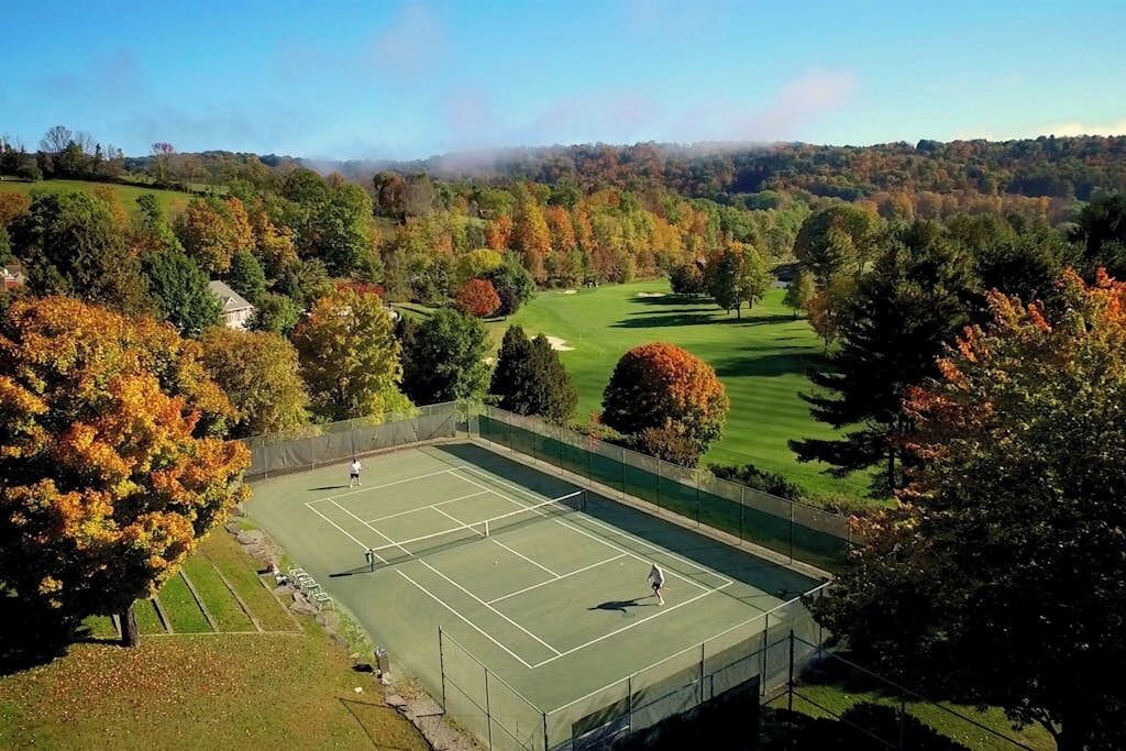 A tennis court surrounded by trees and a golf course in the background.