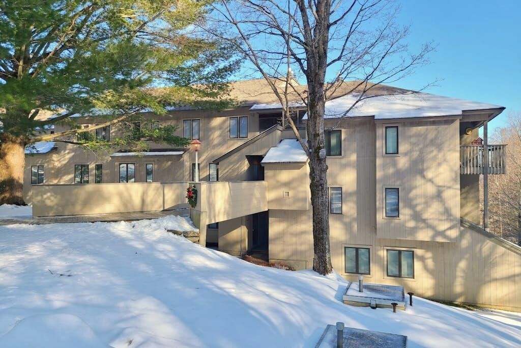 Un edificio a più piani con il terreno innevato, una scala che porta a un balcone e una panchina in primo piano.