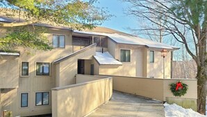 Un immeuble à plusieurs étages doté d’une terrasse en bois menant à l’entrée, d’un escalier et d’une guirlande accrochée au mur.