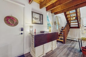 A room with a wooden staircase, a white door, a dark wooden counter, and a framed picture on the wall. - Walk-to-village end-unit condo, mountain views, large deck, woodstove, bbq, a/c (Quechee)