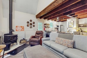 A living room with a sofa, a leather chair, a fireplace, and a kitchen area. - Walk-to-village end-unit condo, mountain views, large deck, woodstove, bbq, a/c (Quechee)
