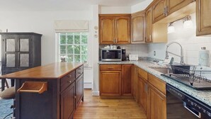 Une cuisine avec des meubles de rangement en bois, un four à micro-ondes, un évier et une fenêtre donnant sur un paysage verdoyant.