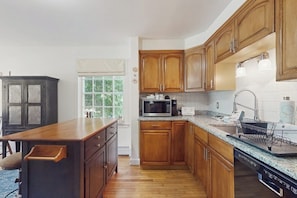 A kitchen with wooden cabinets, a microwave, a sink, and a window with a view of greenery. - Private house w/ seasonal mountain & meadow views, pond, balcony, porch, jacuzzi (Waitsfield)