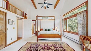 Une chambre à coucher avec un lit à baldaquin, un ventilateur de plafond, une grande fenêtre avec des rideaux et une chaise en bois.