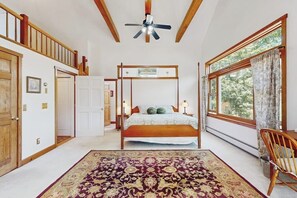 A bedroom with a four-poster bed, a ceiling fan, a large window with curtains, and a wooden chair. - Private house w/ seasonal mountain & meadow views, pond, balcony, porch, jacuzzi (Waitsfield)