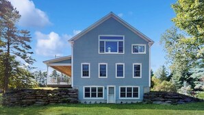 Une maison à deux étages, avec des fondations en pierre, un porche et un ciel dégagé.