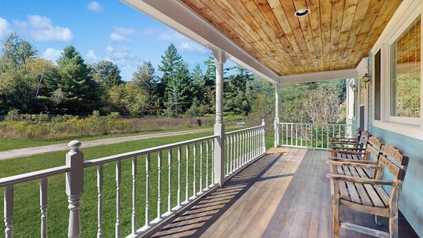 Une terrasse en bois avec des rampes blanches, des bancs en bois et une vue sur un paysage verdoyant.