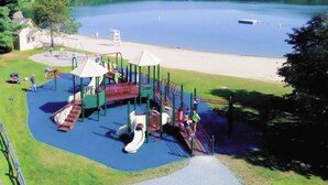A playground with slides and climbing structures near a lake. - Inviting three-story condo with decks  - near the Quechee Club (White River Junction)