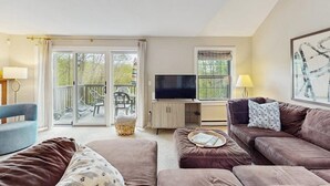 A living room with a sofa, a television, and a window with curtains. - Inviting three-story condo with decks  - near the Quechee Club (White River Junction)