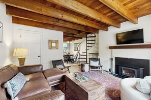 A living room with a fireplace, leather sofas, a coffee table, and a TV mounted on the wall. - Quechee condo, outdoor activities nearby, kitchen, TV, wifi (Quechee)