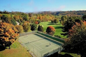 A tennis court surrounded by trees and a golf course in the background.