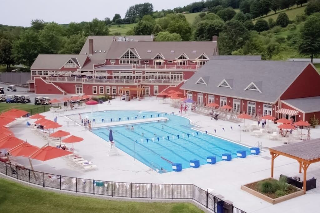 Una grande piscina con più corsie, circondata da una zona coperta con ombrelloni rossi.