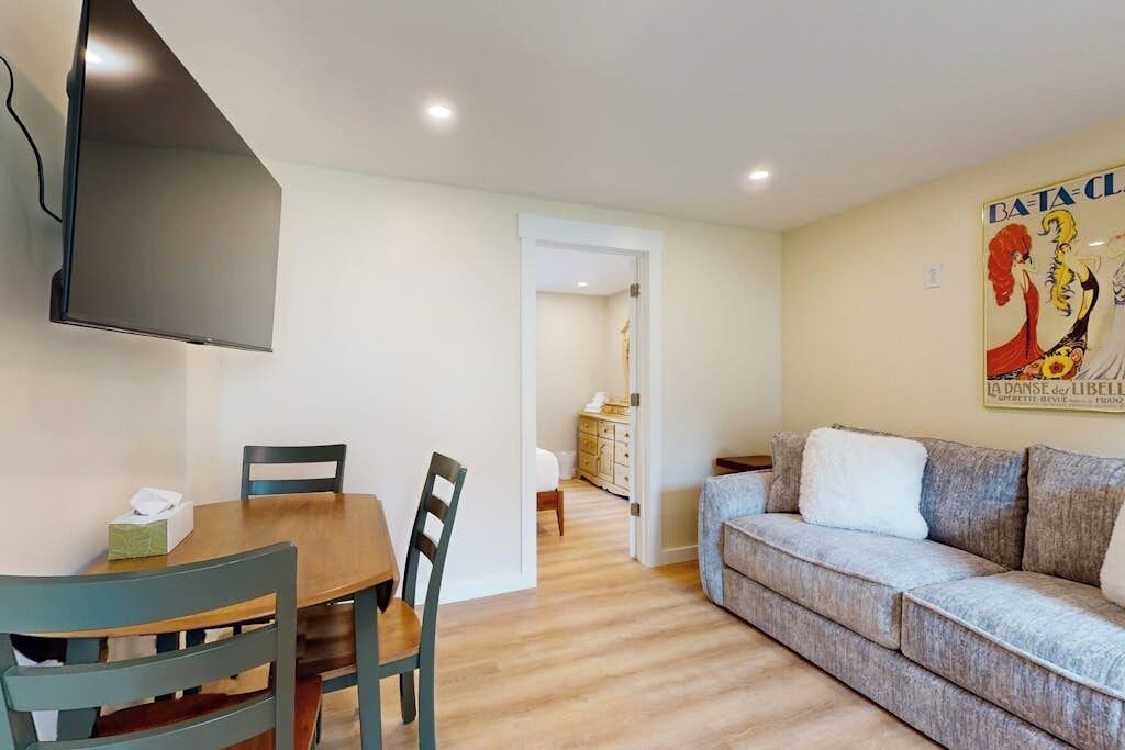 Un salon avec un canapé, une table à manger et des chaises, un téléviseur fixé au mur et une affiche accrochée au mur.