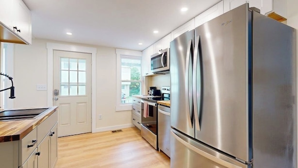 A modern kitchen with stainless steel appliances, wooden flooring, and white cabinetry. - Centrally located apartment for the skier & outdoor enthusiast (Rutland)